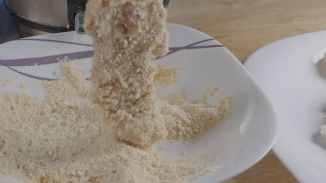 slow motion slider shot of breading chicken breast pieces with a bowl of breadcrumbs in the kitchen