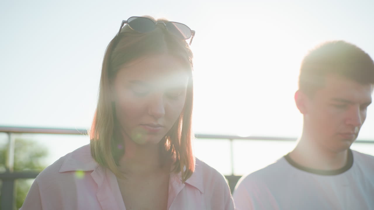 머리에 안경을 쓴 젊은 여성의 클로즈업, 빛에 비추어 반이는 홀로 효과를 만들어, 밖의 레일링에 맞춰 그녀의 에 집중된 젊은 남자와 함께