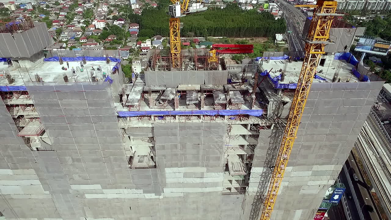 Aerial view of a building construction site with workers assembling the structural framework, machinery in operation, and materials arranged across the work area in an active urban project