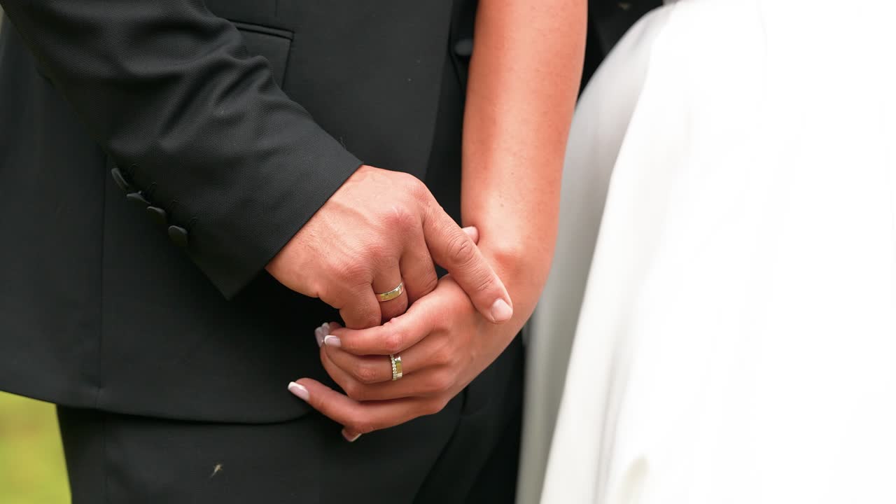 An intimate close-up shot of a couple holding hands, showcasing wedding rings. Captured with natural light, this tender moment is perfect for romance and wedding-themed projects