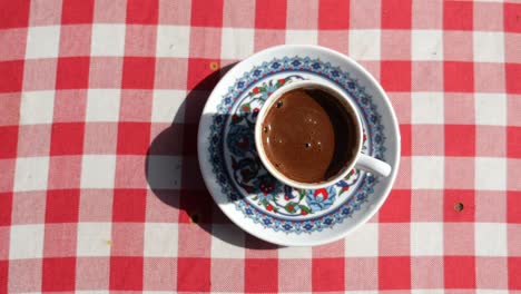 close up of a cup of turkish coffee on a red and white checkered tablecloth