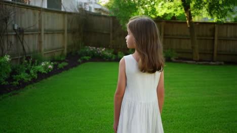 young girl in a white dress standing in a green backyard
