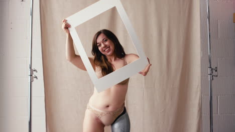 fotografía de estudio de una mujer segura con una prótesis en ropa interior mirando a través del marco de la imagen