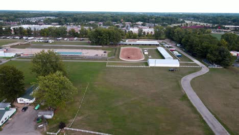 aerial forwarding shot of people riding horse in an outdoor arena during a nice calm day