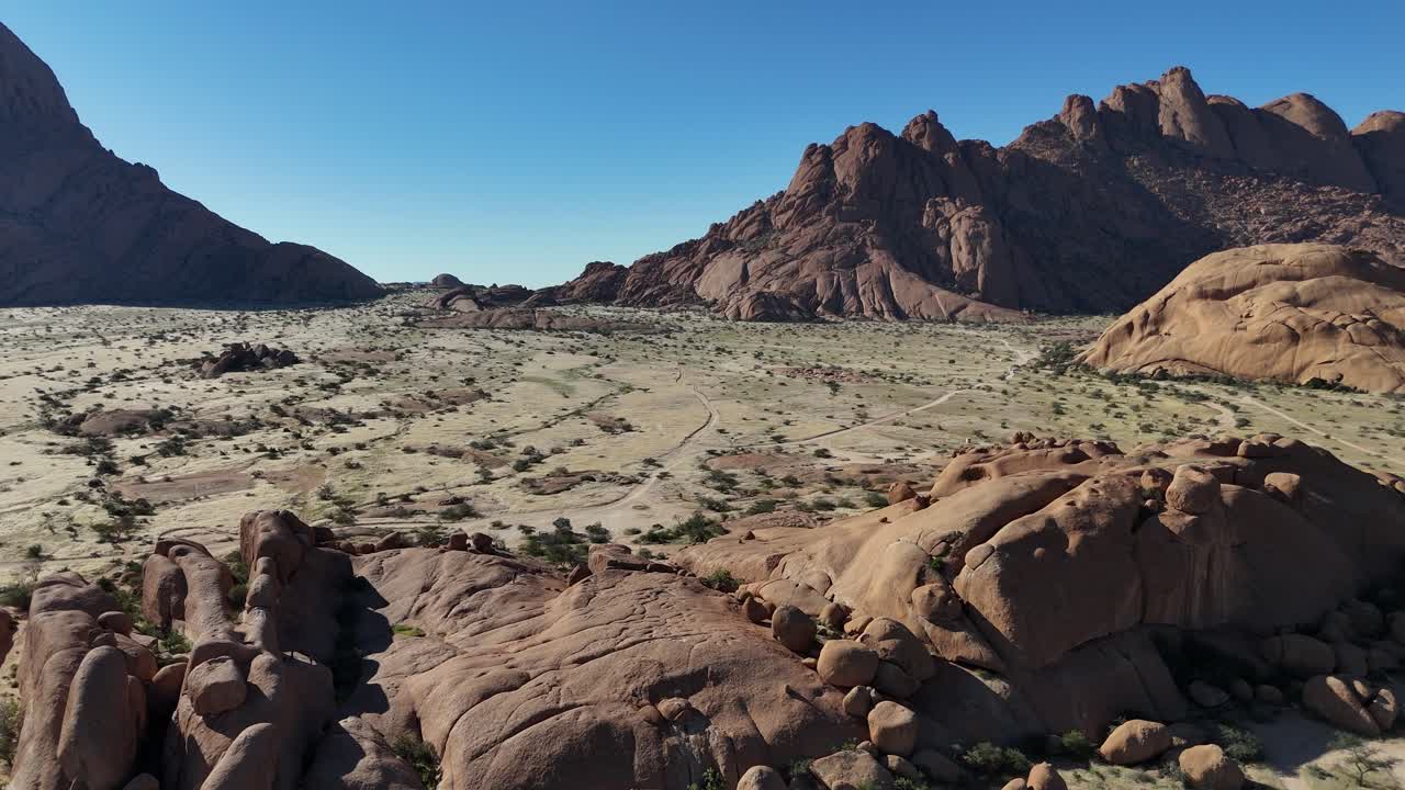 Aerial drone shot over the granite formations of Spitzkoppe in Namibia, revealing the dramatic desert landscape and rocky mountains under a clear blue sky