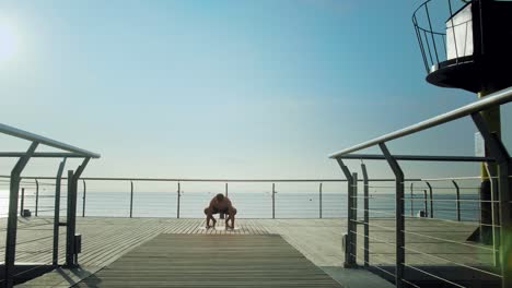 young attractive athlete doing yoga exercises half naked on bridge in the morning and looking into the ocean