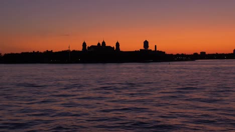 wide hudson river shot, from a boat, showing sailing ship, statue of liberty at dusk, teal and orange sky