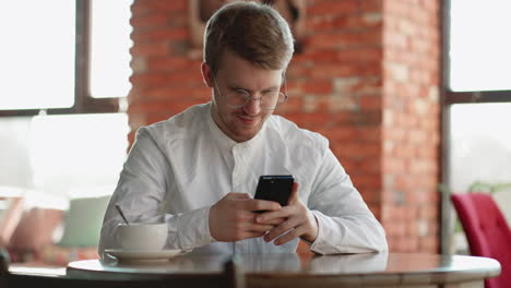 Attraktiver-Mann-Mit-Brille,-Der-Allein-Im-Innenbereich-Steht-Und-Sein-Smartphone-In-Den-Händen-Hält-Und-Die-Nummer-Auf-Dem-Touchscreen-Wählt.-Fröhliche-Junge-Frau,-Die-Auf-Der-Website-Zum-Surfen-Im-Internet-Surft,-Wählt-Das-Online-Konzept-Für-Den-Kauf-Von-Waren