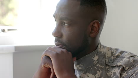 african american soldier in military uniform looks pensive, resting chin on hand at home