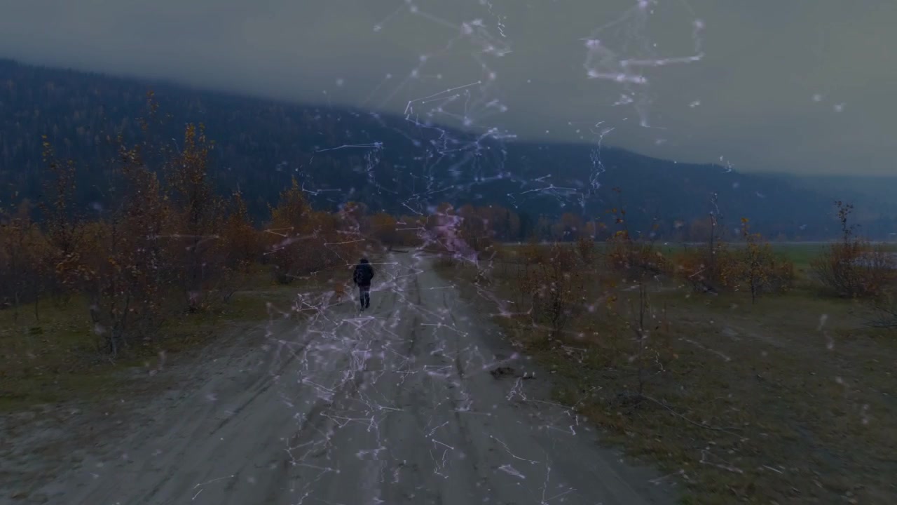 Uomo che cammina dall'orizzonte verso la telecamera su una strada sterrata, con una sovrapposizione di particelle tecnologiche che segue il camminatore