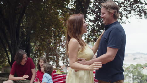 Happy-couple-looking-at-the-camera,-hugging-and-kissing-during-family-picnic