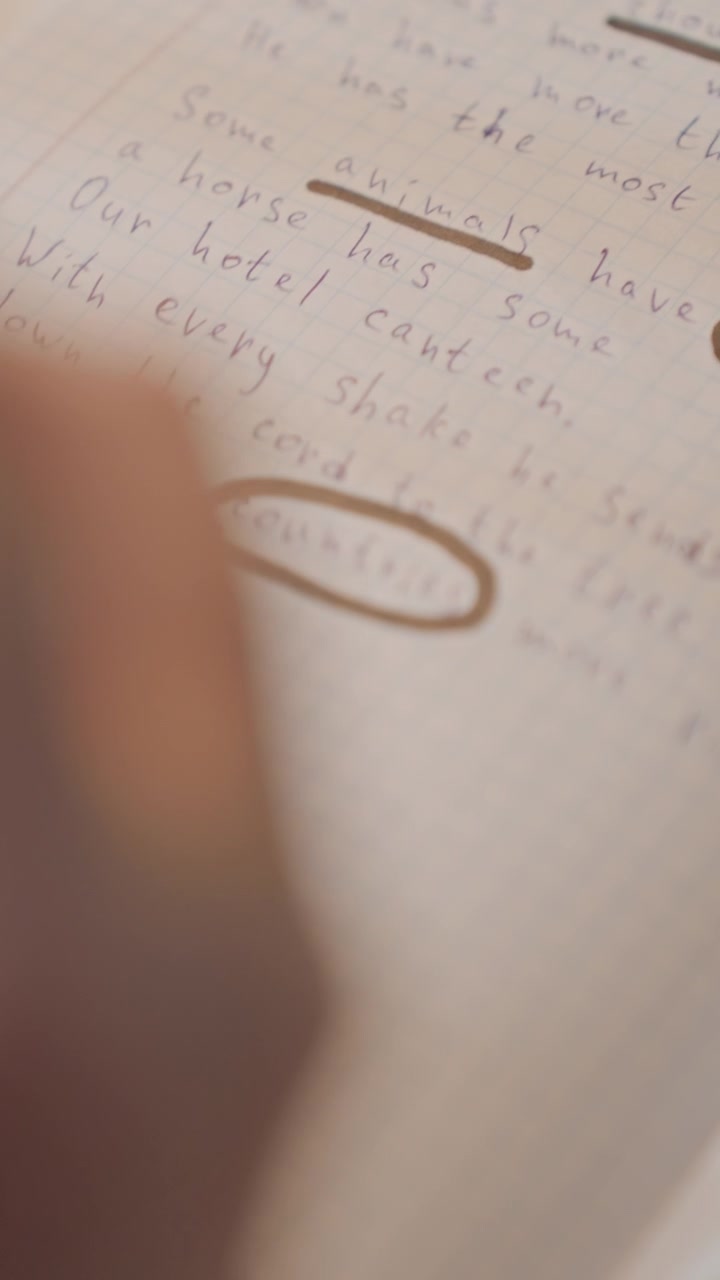 Hand with red sleeve underlines words on lined paper. Camera focuses closely as person highlights specific phrases. Handwritten notes include cursive English writing about animals