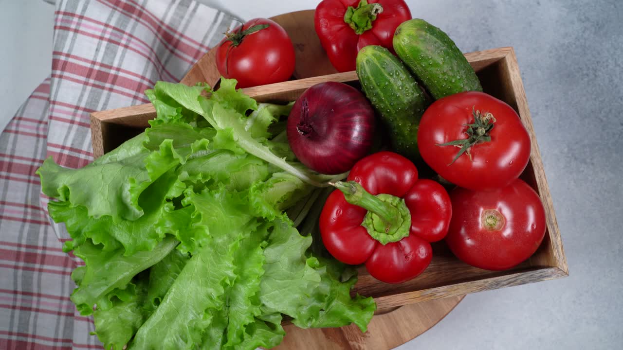 Circular rotation a box with fresh tomato,pepper,green lettuce and cucumber on a plate,top view.