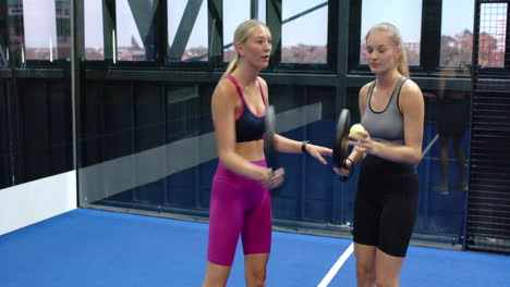 women playing padel tennis, smiling and holding rackets on indoor court