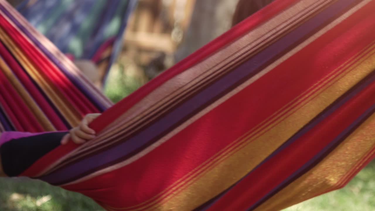 Giovani bambine felici in un campo estivo, sdraiate su amache colorate, si rilassano giocando all'aperto con bambole di peluche a forma di cane in un prato verde. Slow motion di bambini.
