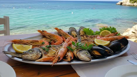 a beautifully arranged seafood platter featuring grilled fish, shrimp, and fresh shellfish served against a stunning coastal background