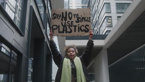 joven activista climático estadounidense sosteniendo una pancarta y protestando contra los plásticos de un solo uso mientras mira la cámara