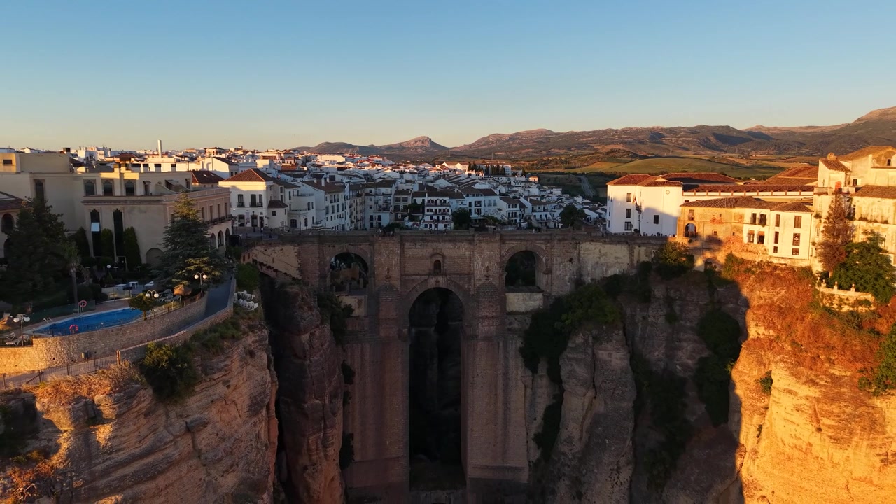 Drone luftfoto af den ikoniske Puente Nuevo-bro, der strækker sig over El Tajo-kløften i Ronda, Spanien, under den gyldne time med dramatisk klippearkitektur
