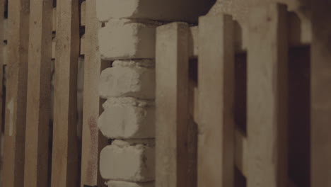 close-up of a textured column, partially obscured by wooden slats, creating an interplay of shadows and architectural detail in a muted color palette