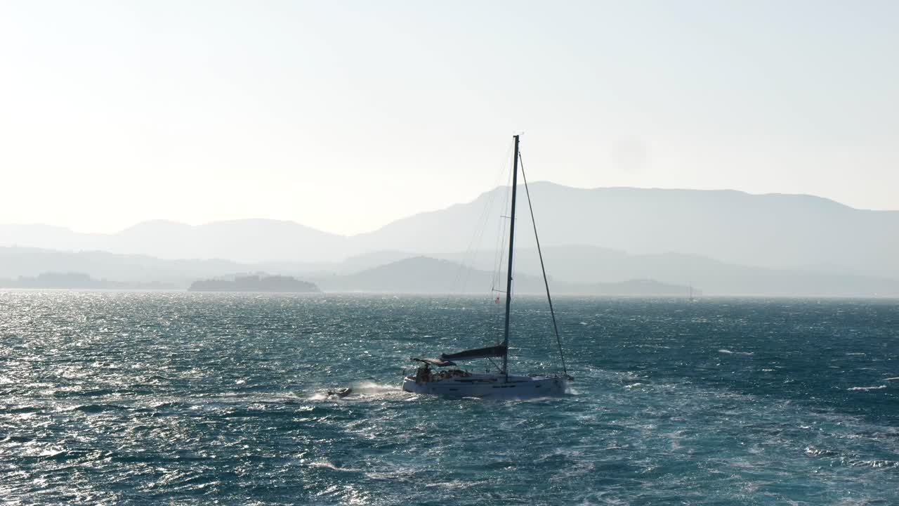 barco de vela que navega a través de las aguas turbulentas del mar jónico cerca de la isla de corfú, remolcando un pontón