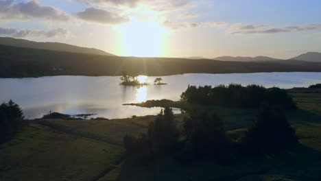 aerial backlit static establishing of lough bofin, the last rays of sunlight casting a golden glow over the quiet waters, connemara, galway, ireland