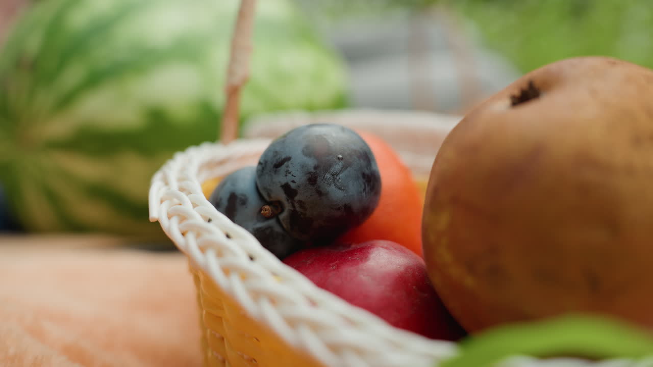 수박 근처 야외 시장에서 짠 바구니에 자두, 오렌지, 사과, 키위를 담고 잘 익은 자두를 고르는 가냘픈 손을 클로즈업한 바구니 신선한 과일, 햇빛이 비치는 가판대 배경, 생생한 색상