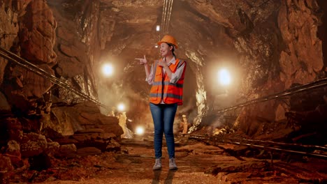 full body of asian female engineer with safety helmet smiling and pointing to side in underground mine tunnel
