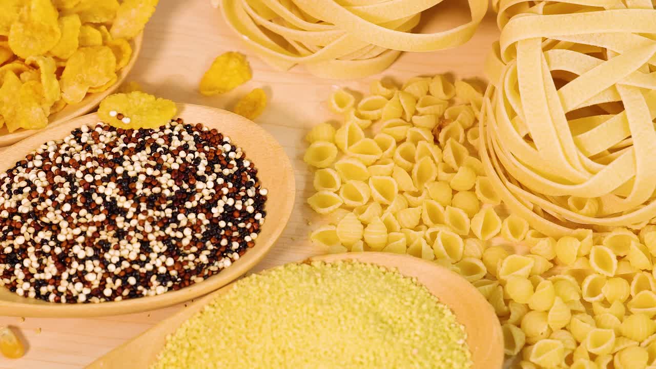 A variety of grains and pasta displayed on a wooden surface with warm lighting, showcasing different textures and shapes