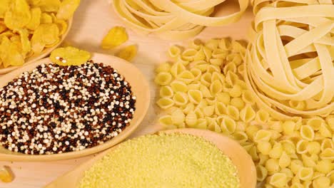 a variety of grains and pasta displayed on a wooden surface with warm lighting, showcasing different textures and shapes