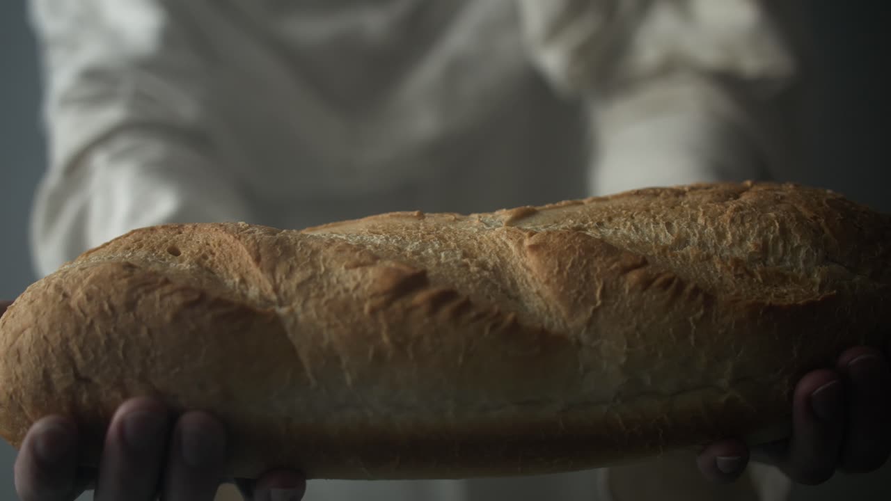 Jesus Christ in white robe and glowing light holding bread and offering it as a representation of the gospel and Jesus as the bread of life in cinematic, dramatic slow motion.