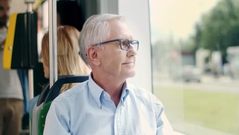 Porträt-Des-Gutaussehenden-älteren-Mannes-Mit-Brille,-Der-In-Die-Straßenbahn-Fährt,-Sitzt-Und-In-Das-Fenster-Schaut,-Der-In-Die-Kamera-Lächelt