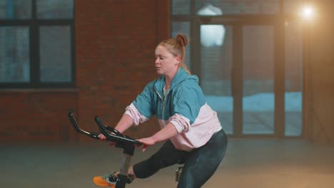 Healthy-Caucasian-woman-exercising-workout-on-stationary-cycle-machine-bike-in-gym,-Slow-Motion