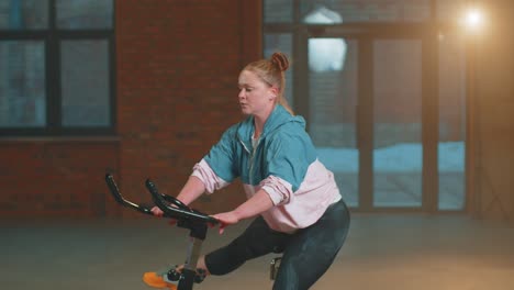 healthy caucasian woman exercising workout on stationary cycle machine bike in gym, slow motion