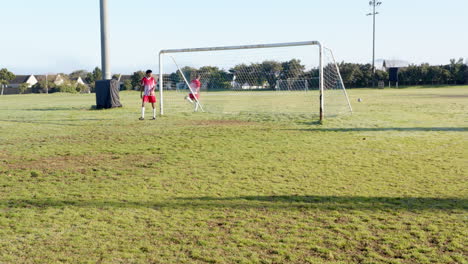 playing soccer on field, players in red uniforms practicing goalkeeping and shooting