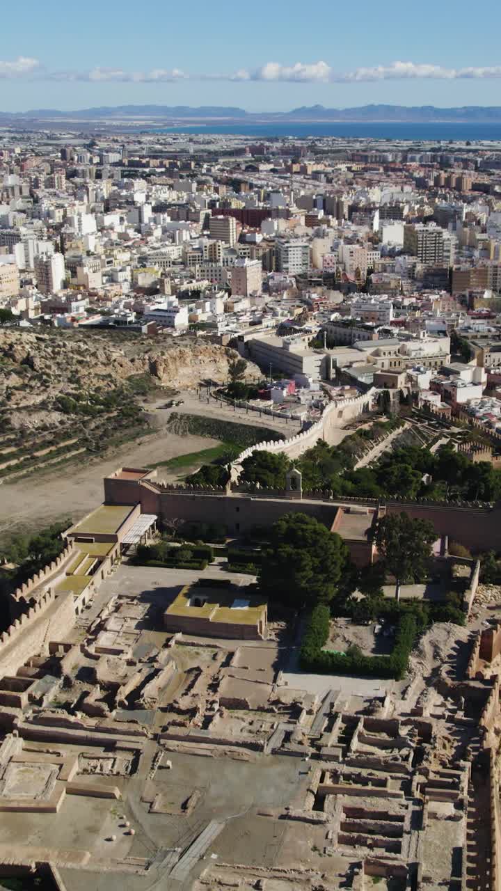 Vista aerea verticale frontale che sorvola l'Alcazaba fortificata di Almería, con il Mar Mediterraneo blu visibile sullo sfondo