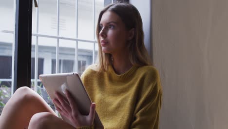 Frau-Benutzt-Digitales-Tablet,-Während-Sie-Zu-Hause-Am-Fenster-Sitzt