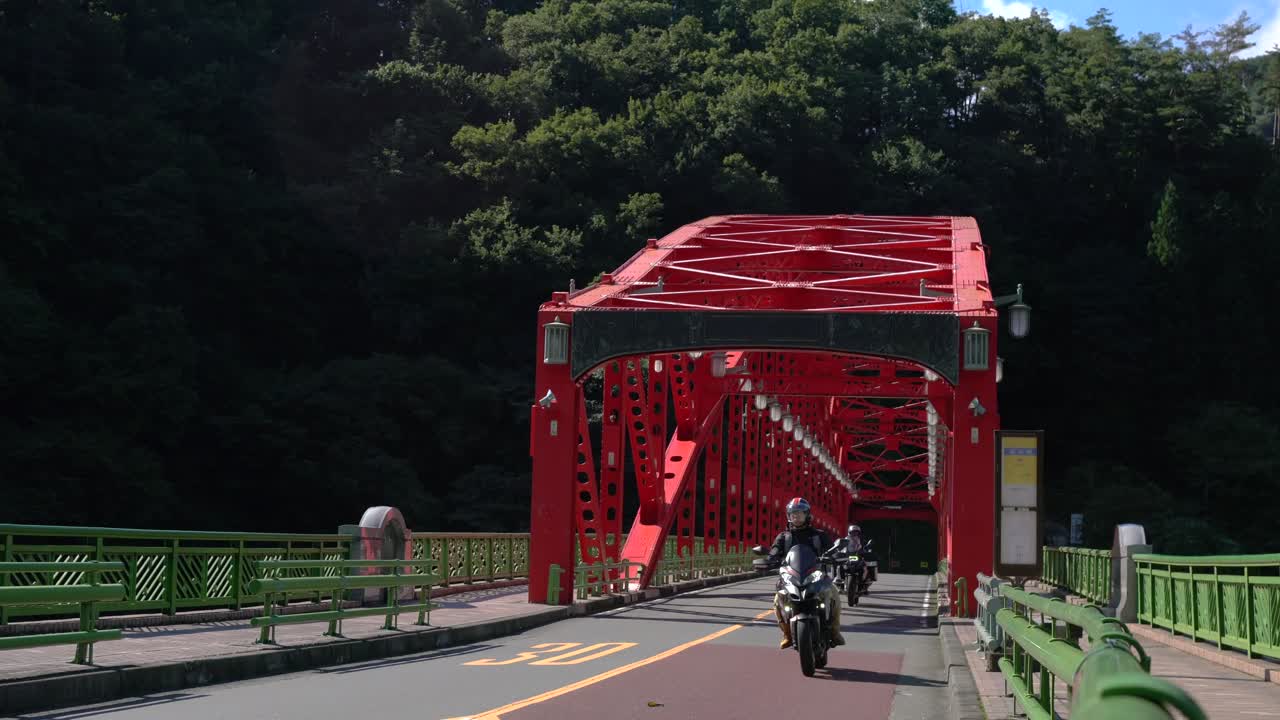 scenic view of 2 motorcycles crossing iconic red bridge in Lake Okutama, nature getaway located in west Tokyo