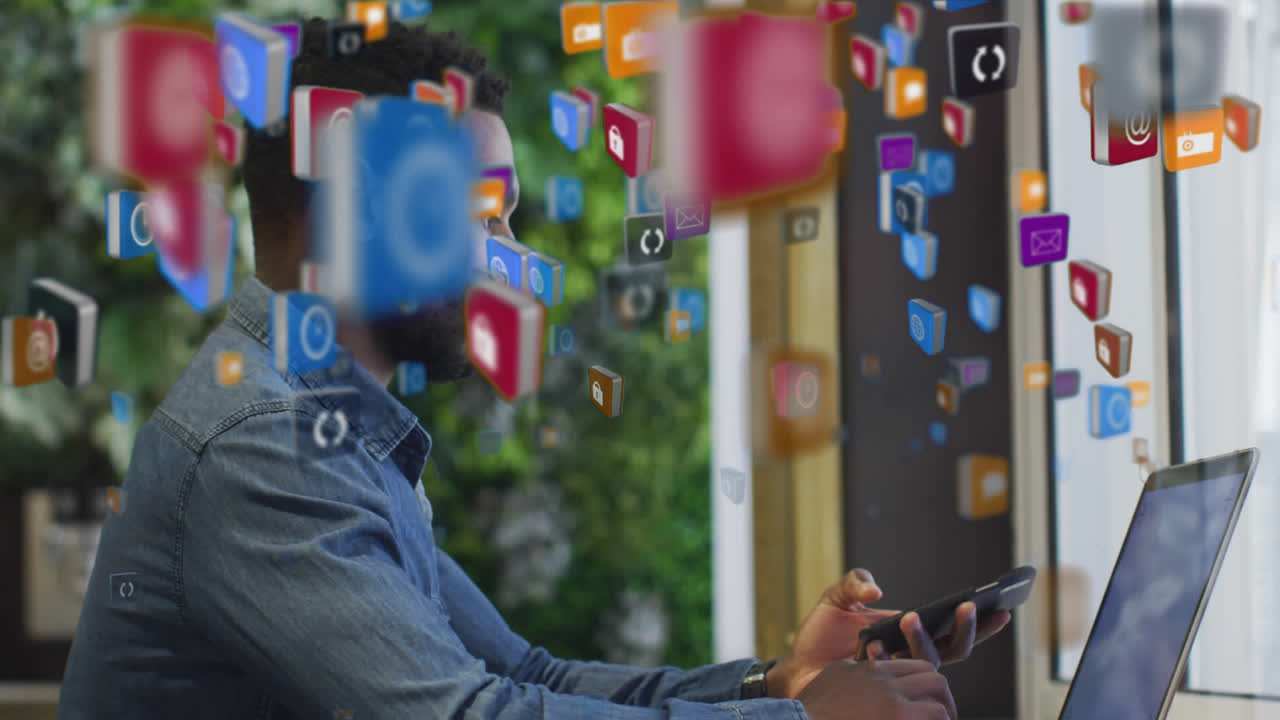 vários ícones digitais flutuando contra um homem afro-americano usando laptop e smartphone