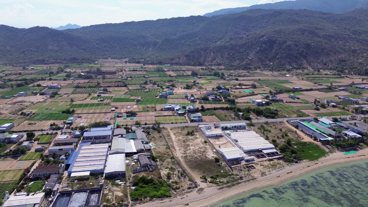 Aerial pan right over "My Hoa" Lagoon in Phan Rang, Vietnam, showcasing the shoreline, shallow waters and agricultural land.