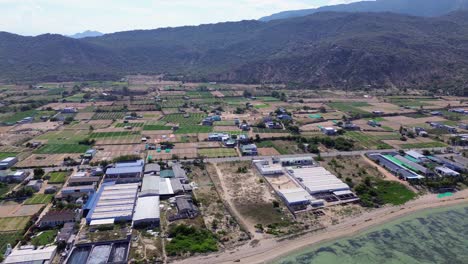 Aerial pan right over "My Hoa" Lagoon in Phan Rang, Vietnam, showcasing the shoreline, shallow waters and agricultural land.
