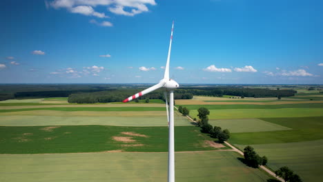 Spinning-wind-turbine-in-green-farm-lands-with-stunning-blue-sky,-aerial-arc