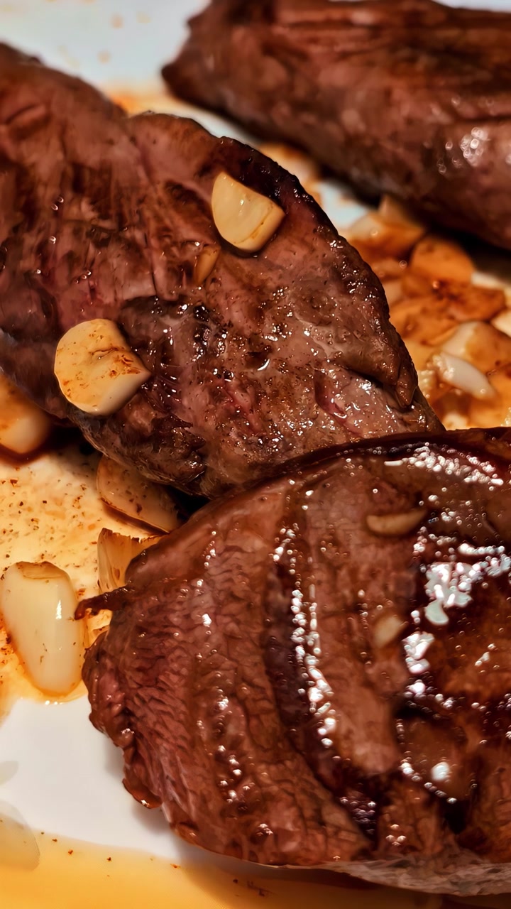 Macro shot of tender grilled beef medallions topped with aromatic roasted garlic. Authentic cinematic food presentation for culinary and restaurant marketing.