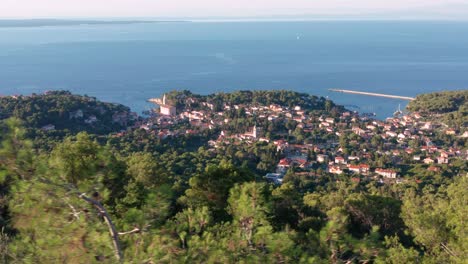 overflying the lush green mountains overlooking the seaside village of veli losinj and northern adriatic sea on a sunny summer day in losinj island, western croatia