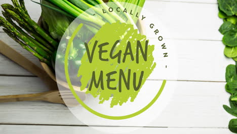 animation of locally grown vegan menu text in green, over bowl of fresh vegetables on white boards