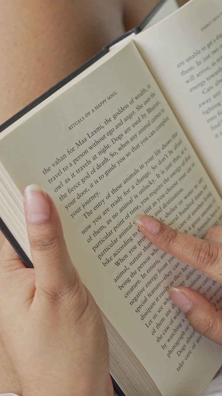 Close-up of a woman's hand gently pressing and smoothing an open book page while reading, with clearly visible printed text and soft natural window light illuminating.