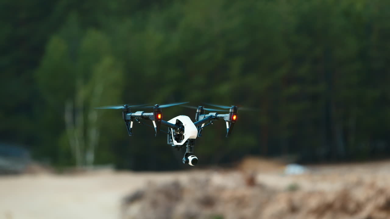 무인 항공기는 모래 사장과 숲의 배경에 대해 공중에 떠 있습니다.