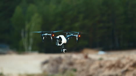 The-drone-hovers-in-the-air-against-the-background-of-the-sandy-shore-and-forest