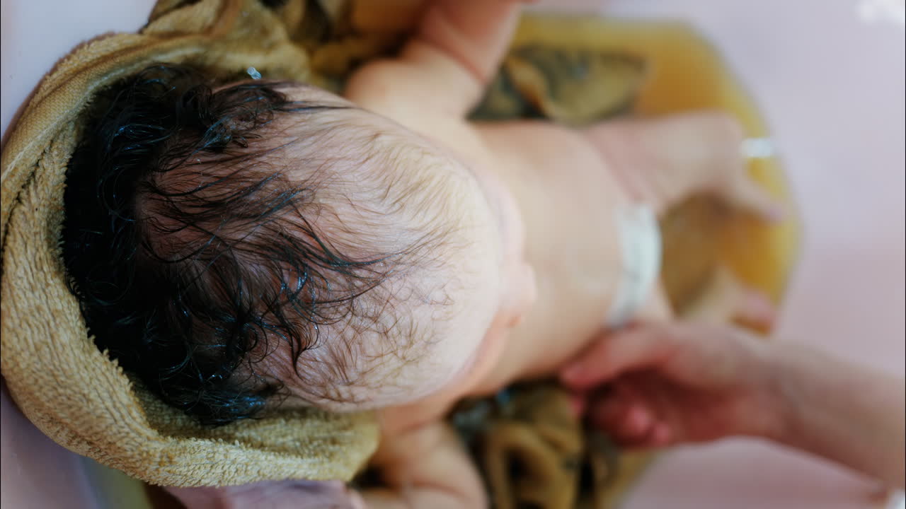 Close up view of a newborn baby being gently bathed by a mother's hand