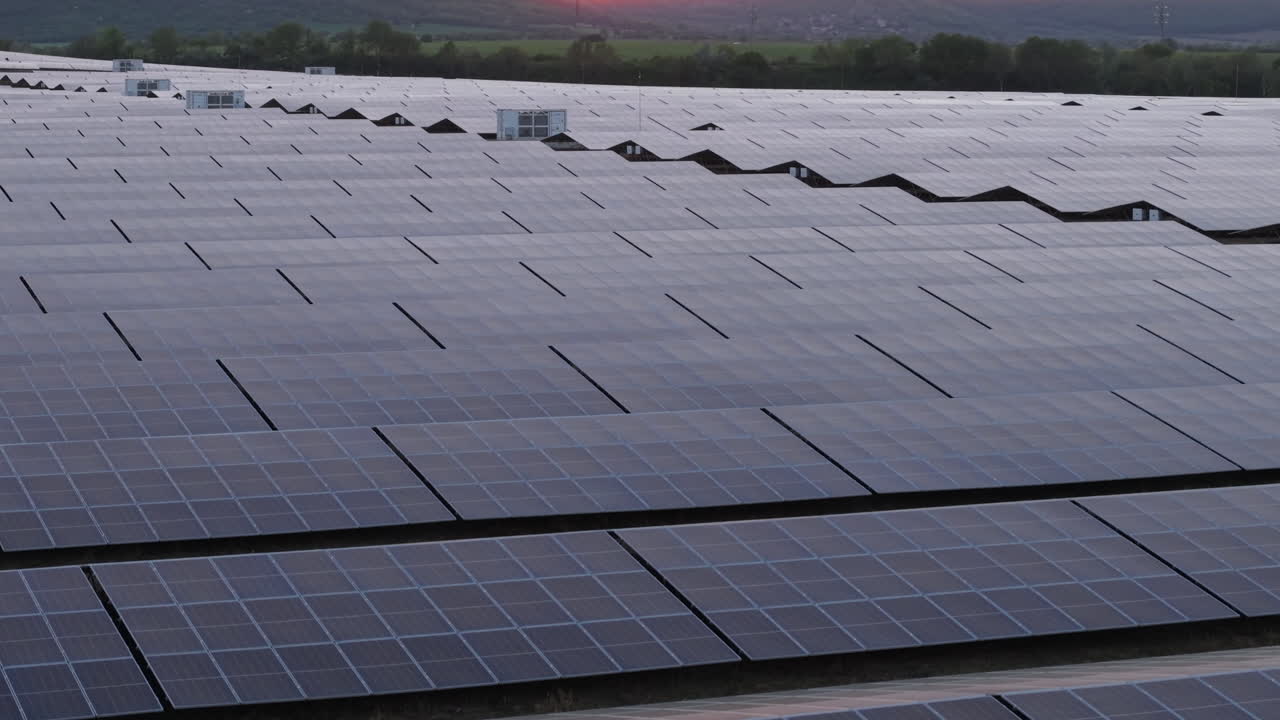 Golden hour aerial shot of a modern photovoltaic solar park in Bulgaria. Rows of solar panels stretch across the open landscape, reflecting warm sunset light