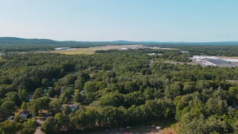 Eine-4K-Drohnenaufnahme-Eines-Waldes-Mit-Häusern-Und-Einer-Stadt-In-Der-Nähe-Mit-Land